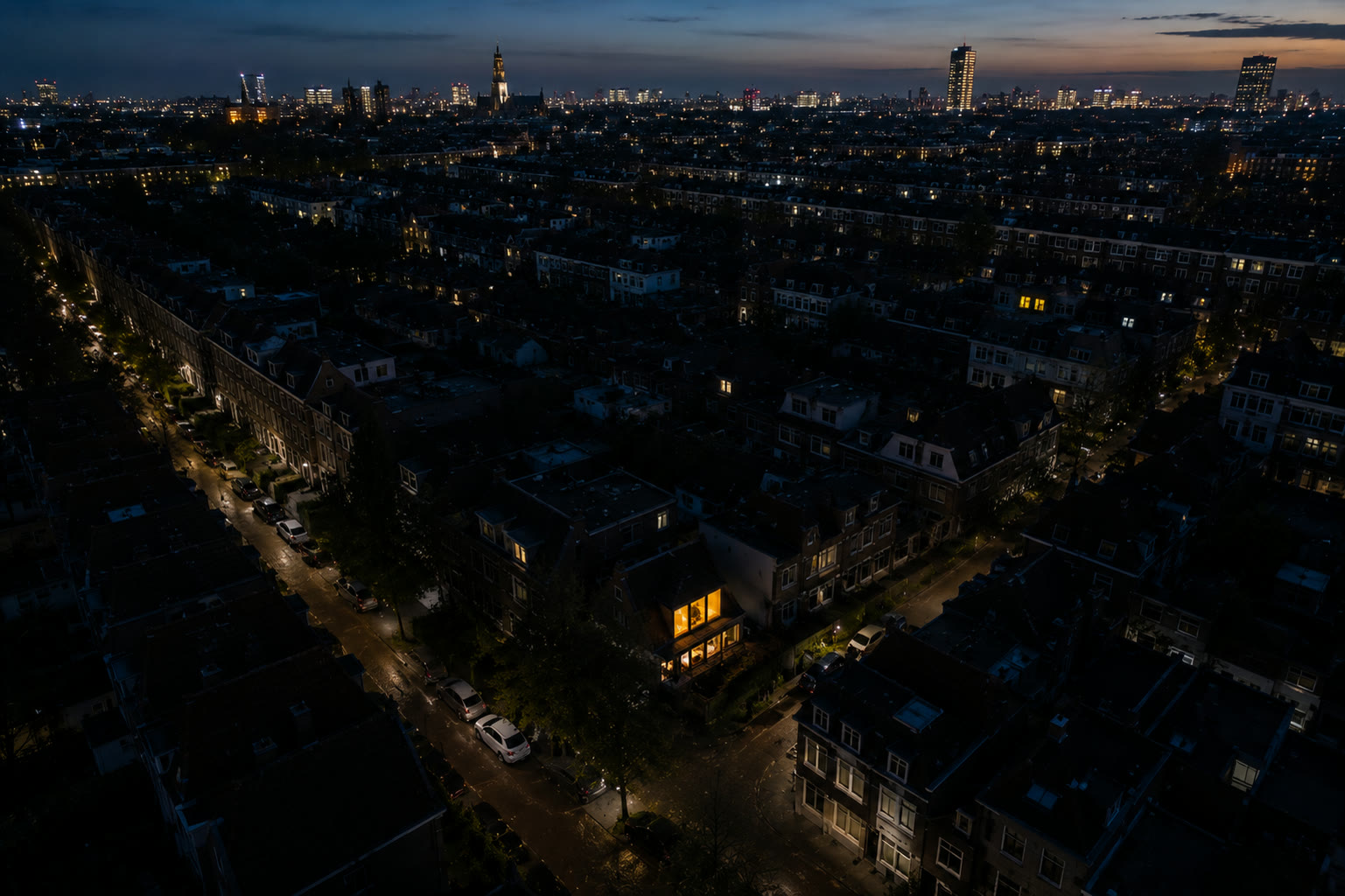 Een donkere stad bij nacht waar midden in de wijk bij één huis het licht warm brandt